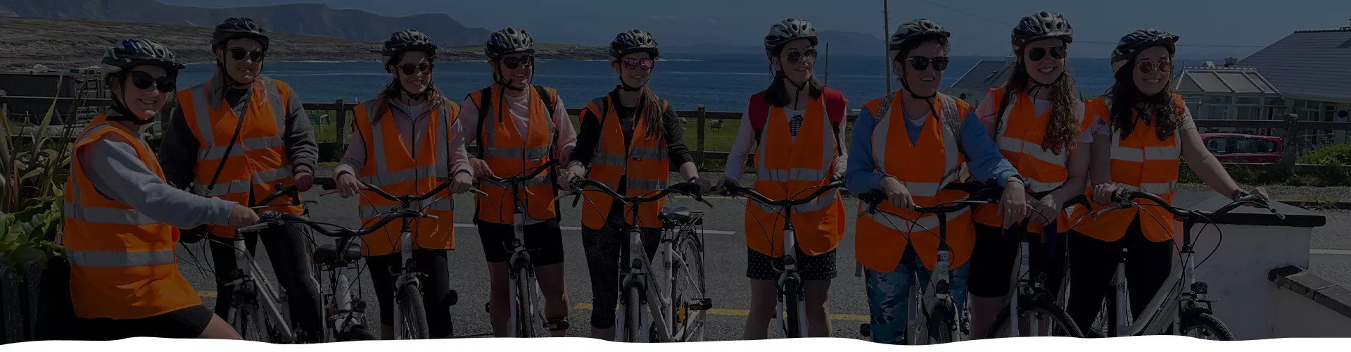 A group of cyclists in safety gear and orange vests standing together outdoors.