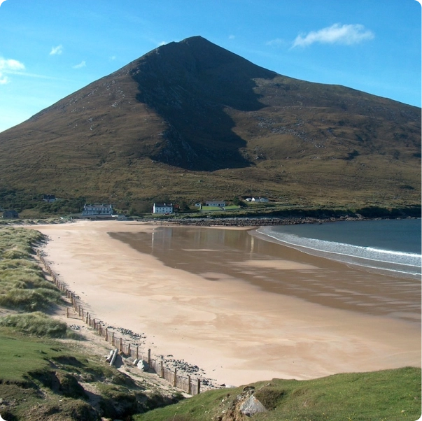 A large mountain overlooking a sandy beach with a few buildings near the shore.