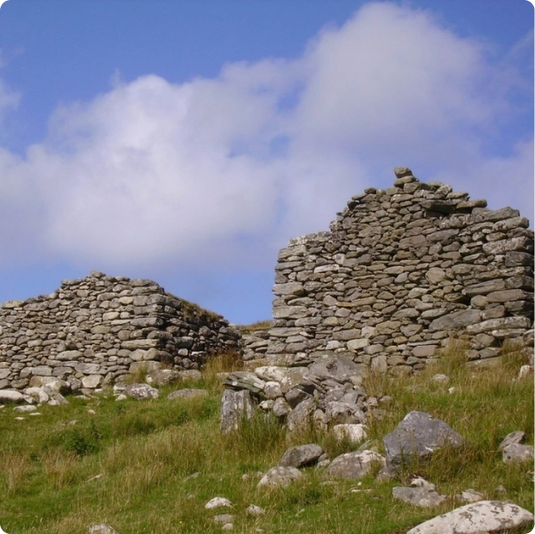 Ancient stone ruins on a grassy hill under a blue sky with scattered clouds.