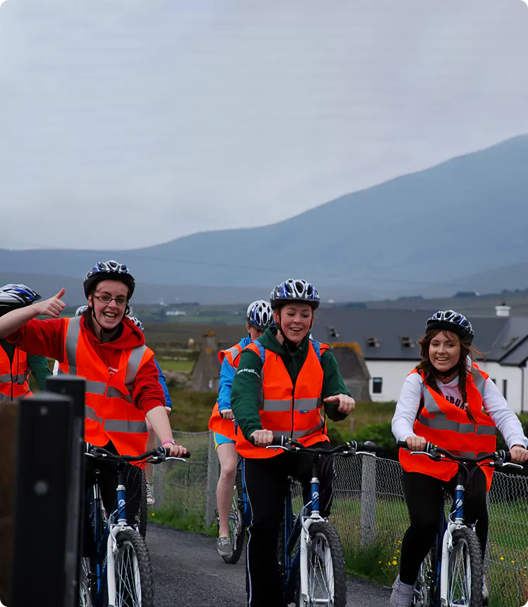 Group of cyclists in reflective vests and helmets smiling while riding bikes in a rural area.