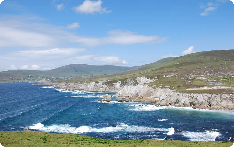 Coastal landscape with rocky cliffs, hills, and blue sea under a clear sky.