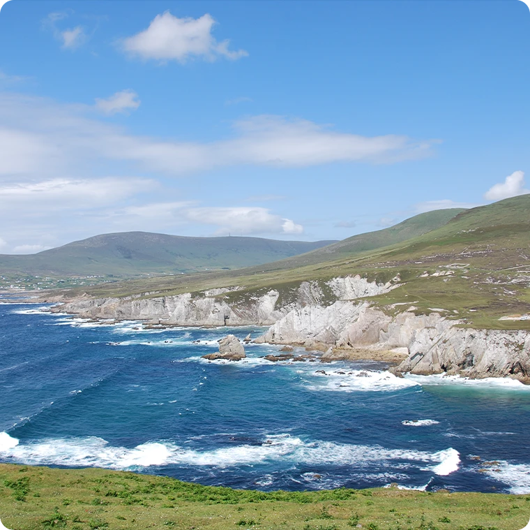 Coastal landscape with blue sea, white cliffs, and green hills under a clear sky.