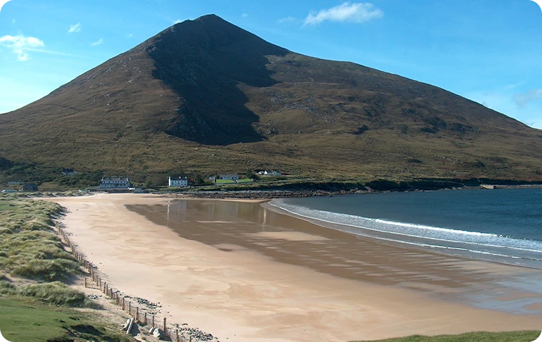 Seaside view featuring a large mountain overlooking a sandy beach with calm waves.