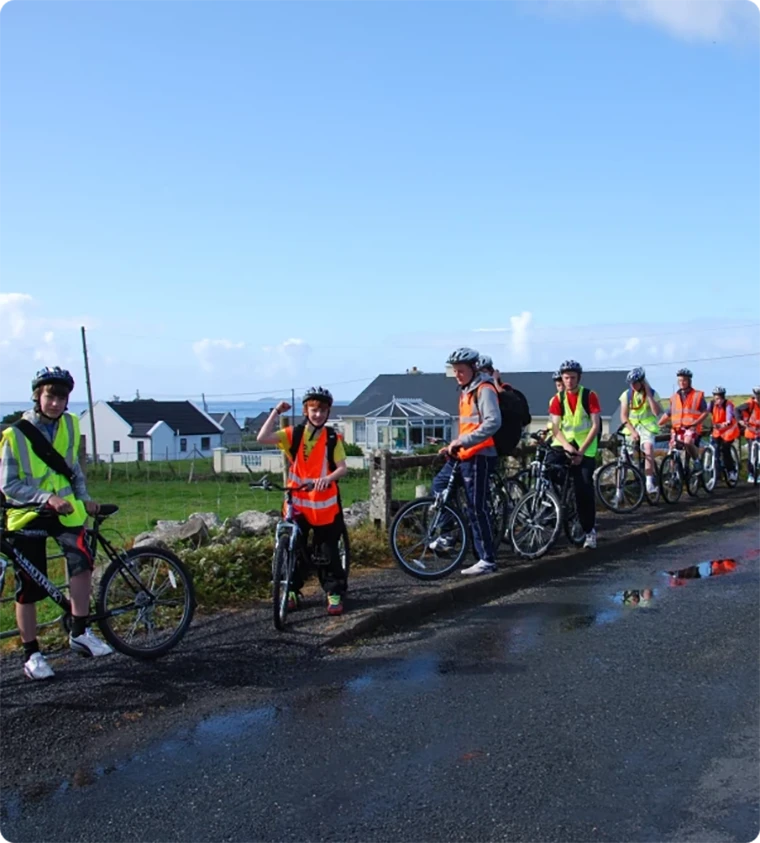 Group of cyclists in hi-vis vests pausing on a sunny road near homes.
