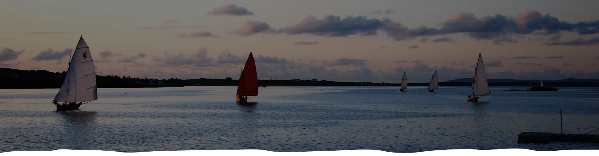 Sailboats with colorful sails on serene water at dusk.