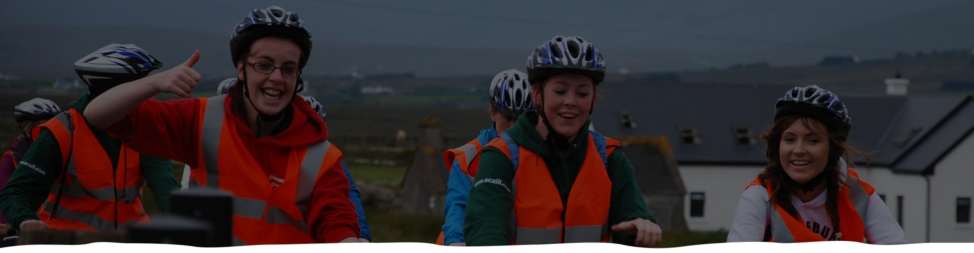 Three cyclists in helmets and reflective vests smiling at dusk.