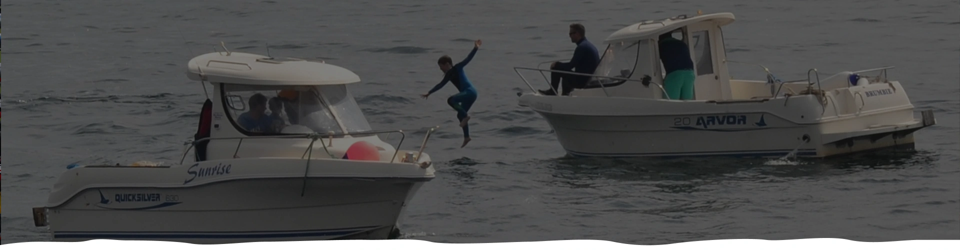 Two boats on water, one person diving from a boat into the sea.